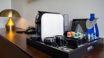 Una estación de café con cafetera, tazas, una botella de agua y un vaso.