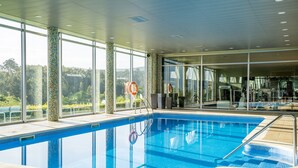 An indoor swimming pool with clear glass walls, a tiled floor, and a view of the outdoors.