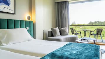 Ett hotellrum med en säng, en soffa, ett bord och stolar. Det finns ett fönster med utsikt över ett grönskande landskap.