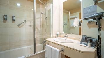 A modern bathroom with a glass-enclosed shower, a sink with toiletries, and a hairdryer mounted on the wall.