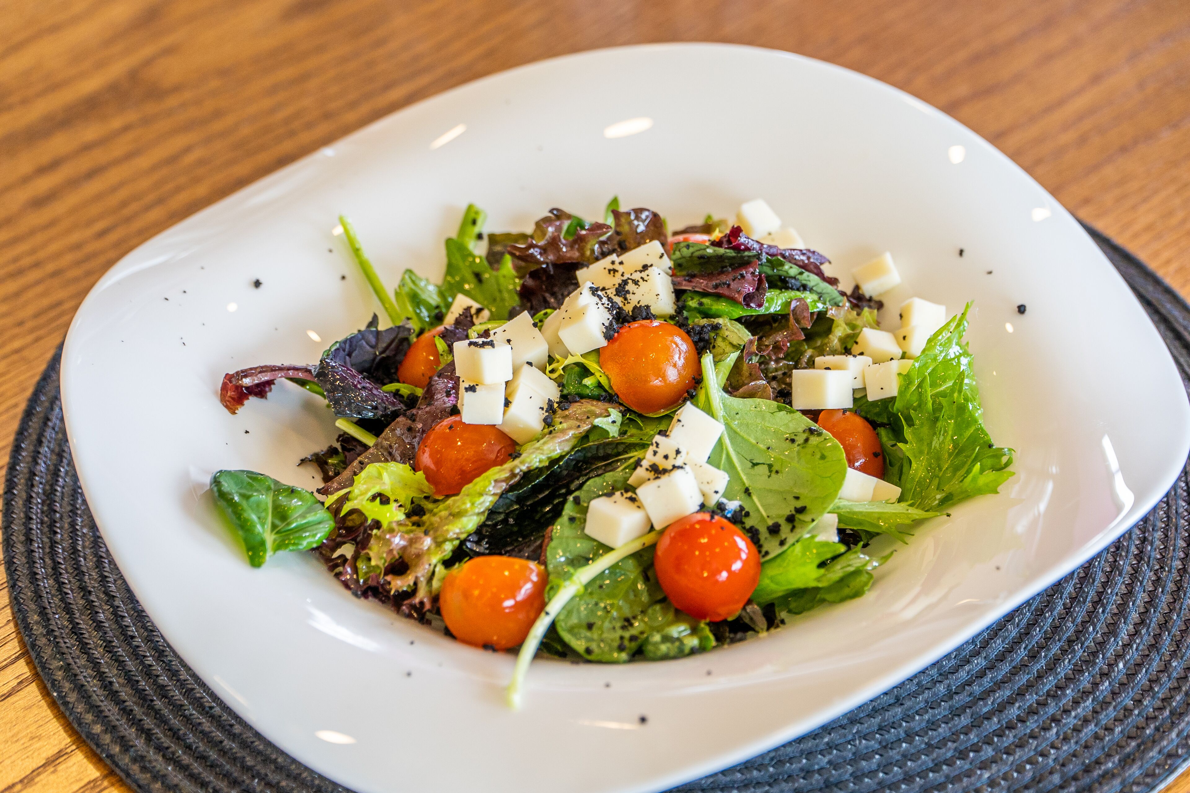 A white plate with a salad containing lettuce, cherry tomatoes, and cubes of cheese.