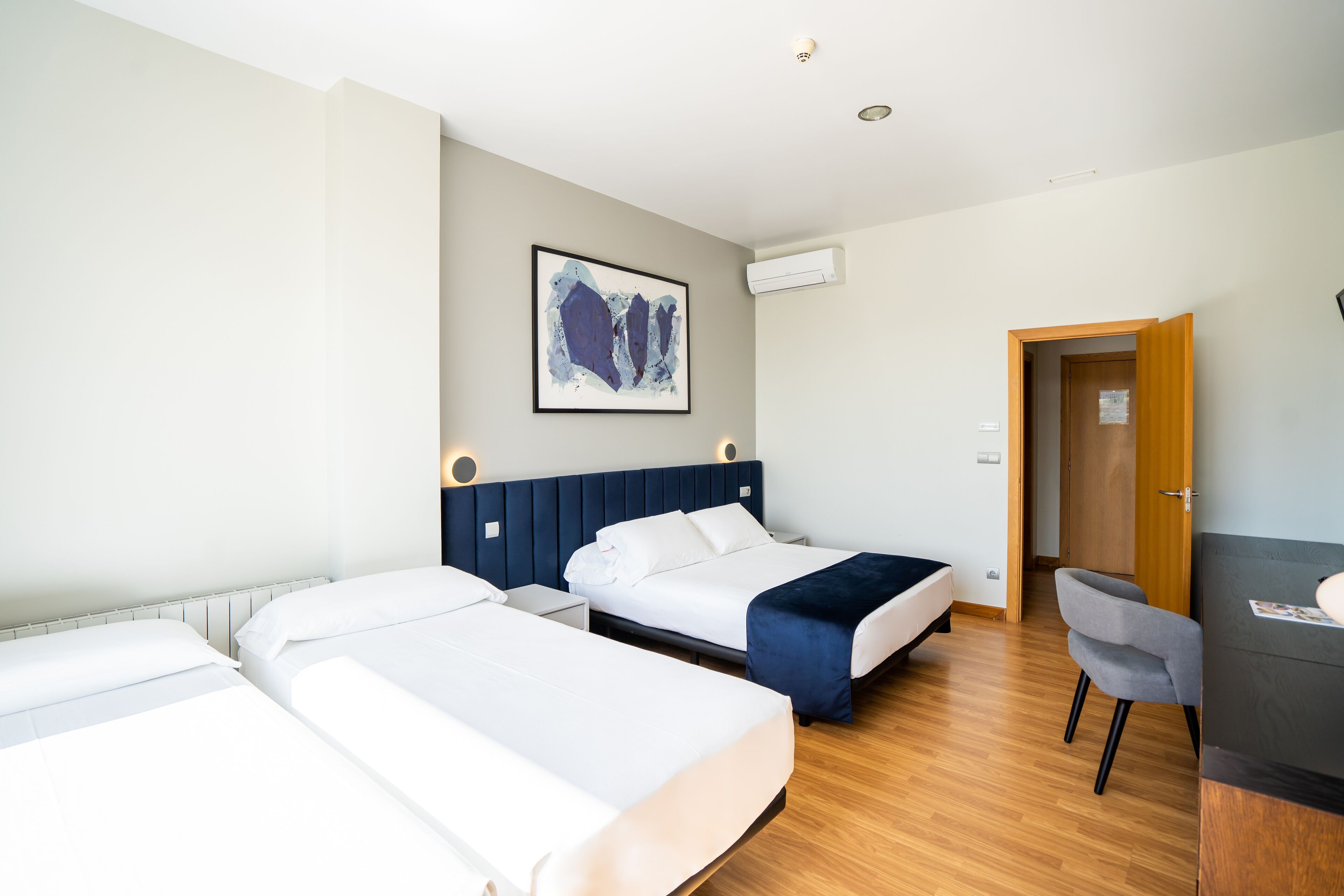 Habitación de hotel con dos camas, un escritorio, una silla y un cuadro en la pared.