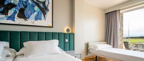 A hotel room with a large bed, a smaller bed, a painting on the wall, and a view of the outdoors through a window.