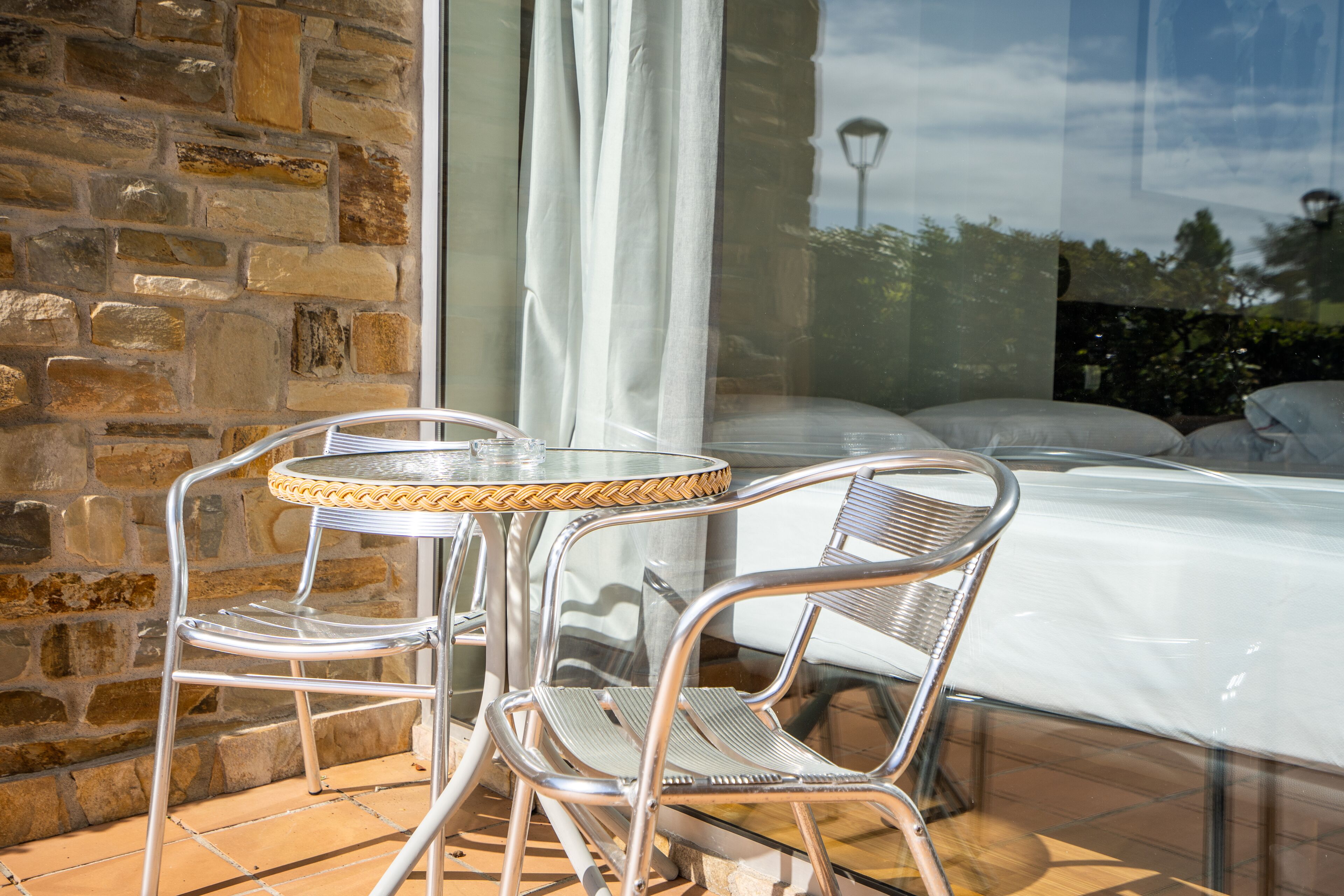 A room with a stone wall, a glass door, a bed, and a small round table with chairs.