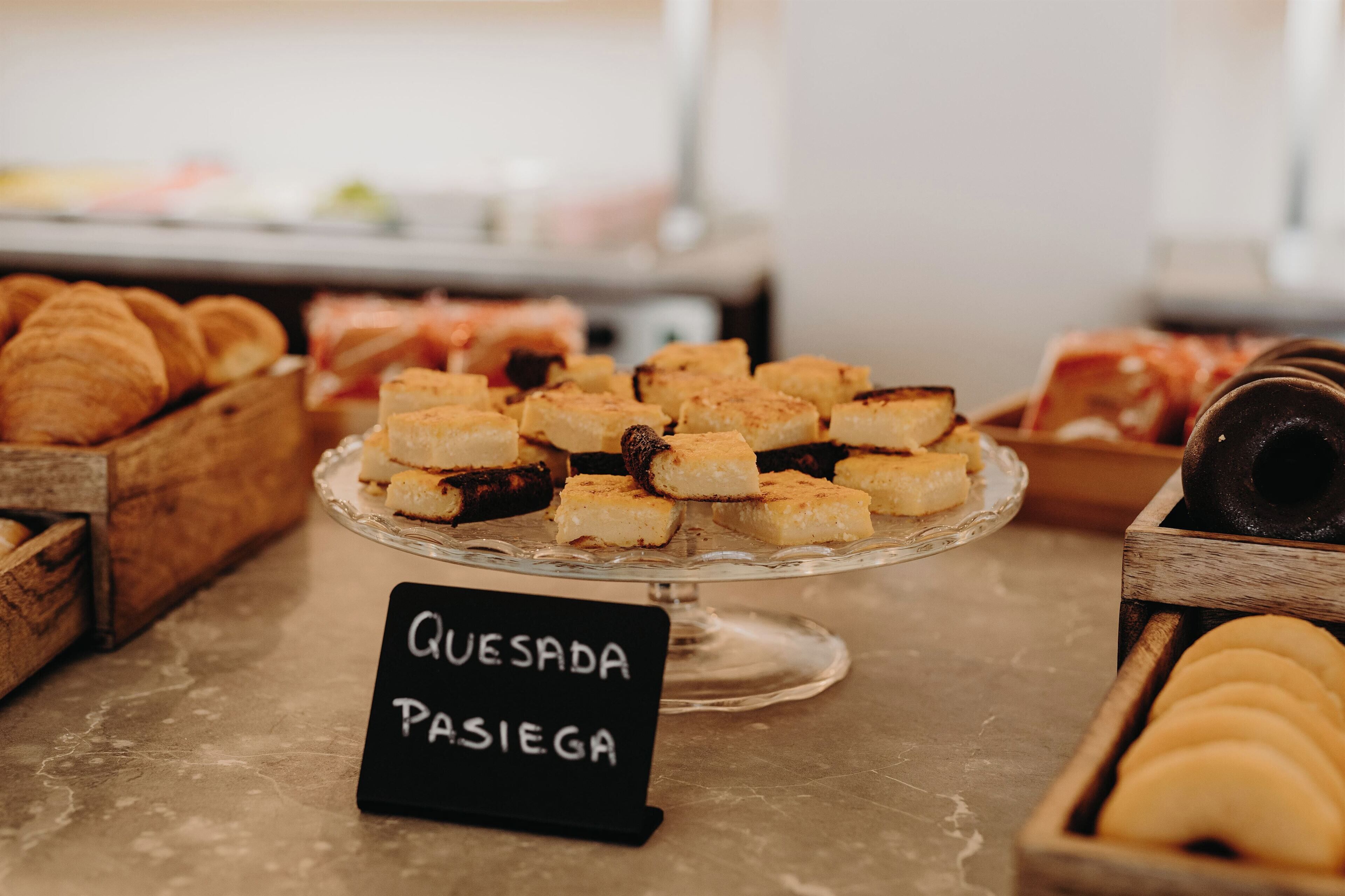 A display of pastries and bread, including a sign labeled "Quesada Pasiega".