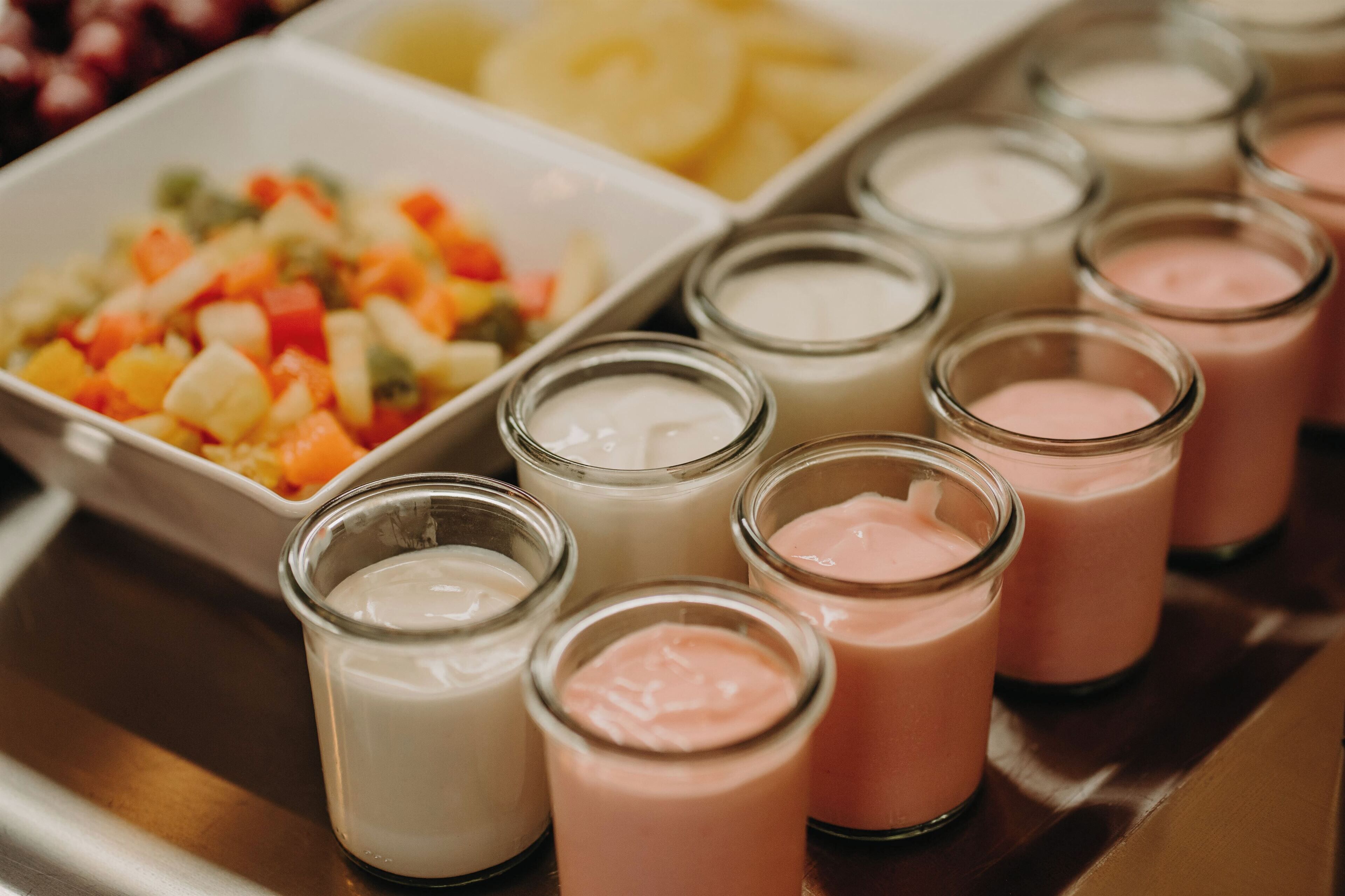 A tray with various food items including a fruit salad and several small glasses of different colored beverages.