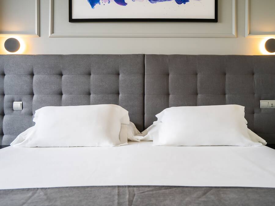 A neatly made bed with white linens and a grey tufted headboard.