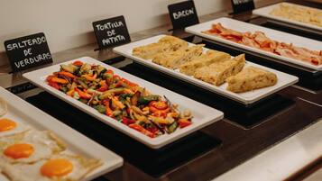 A buffet with labeled dishes including 'Salteado de Verduras', 'Tortilla de Patatas', and 'Bacon'.