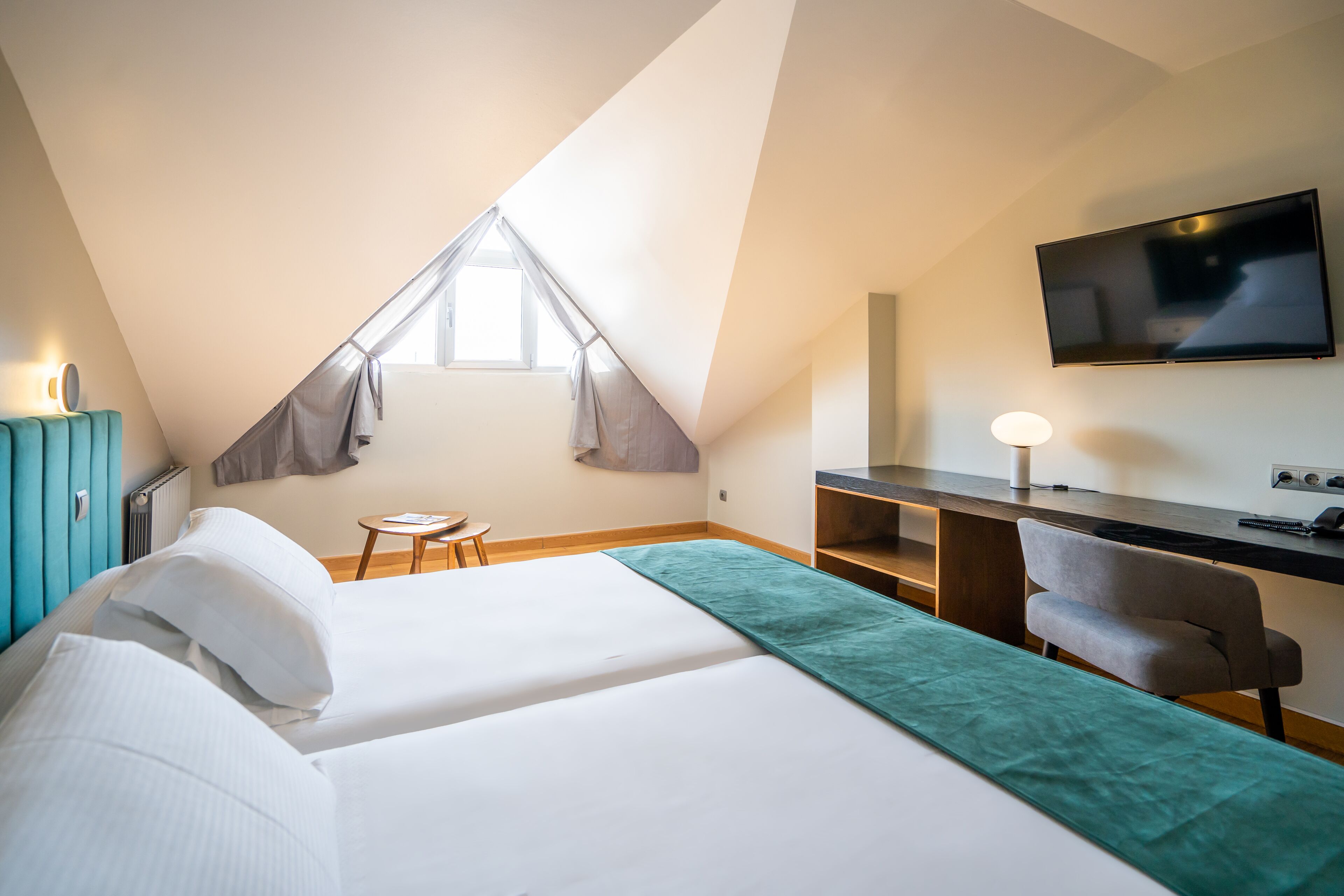 A bedroom with a bed, a desk, a chair, a TV, and a window.