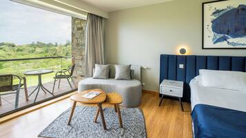 Una habitación de hotel moderna con balcón, un sofá, una cama, una mesita y una mesita de noche.