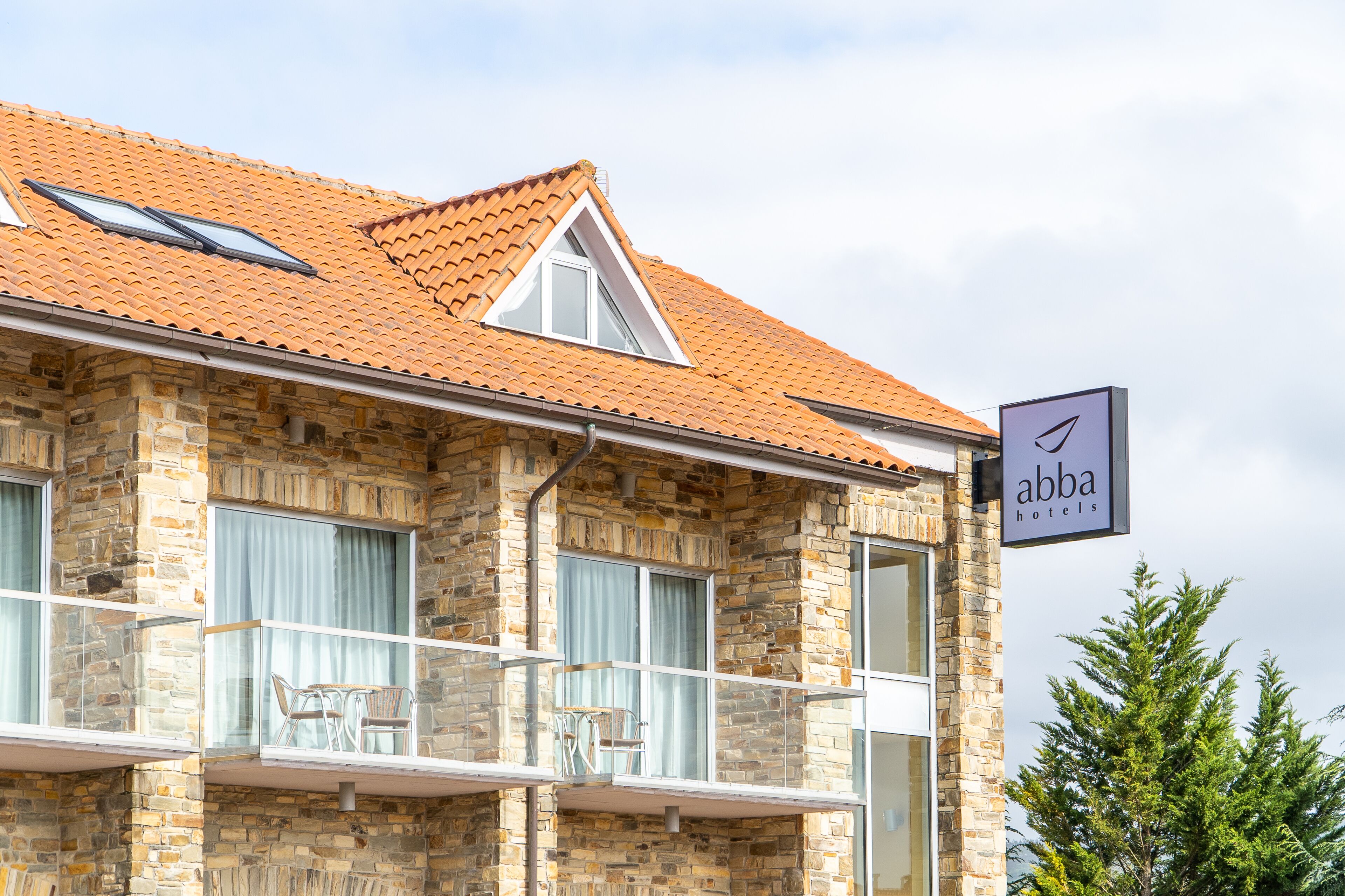 A stone building with a tiled roof, a balcony with chairs, and a sign for Abba Hotels.