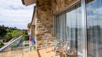 A balcony with stone walls, a glass table, wicker chairs, and a view of greenery and buildings.