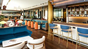 A modern bar area with blue seating, a wooden bar counter, and a variety of bottles. - Radisson Blu Media Harbour Hotel, Düsseldorf (Düsseldorf)