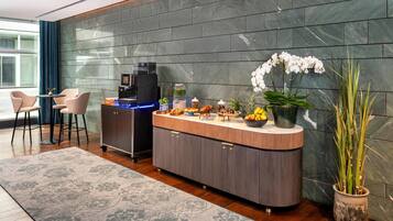 Un espace d’accueil moderne doté d’un comptoir incurvé, d’un espace dédié à la préparation de boissons, d’un coin salon et de plantes décoratives.
