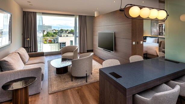 A modern living room with a sofa, chairs, a coffee table, and a TV. - Radisson Blu Media Harbour Hotel, Düsseldorf (Düsseldorf)