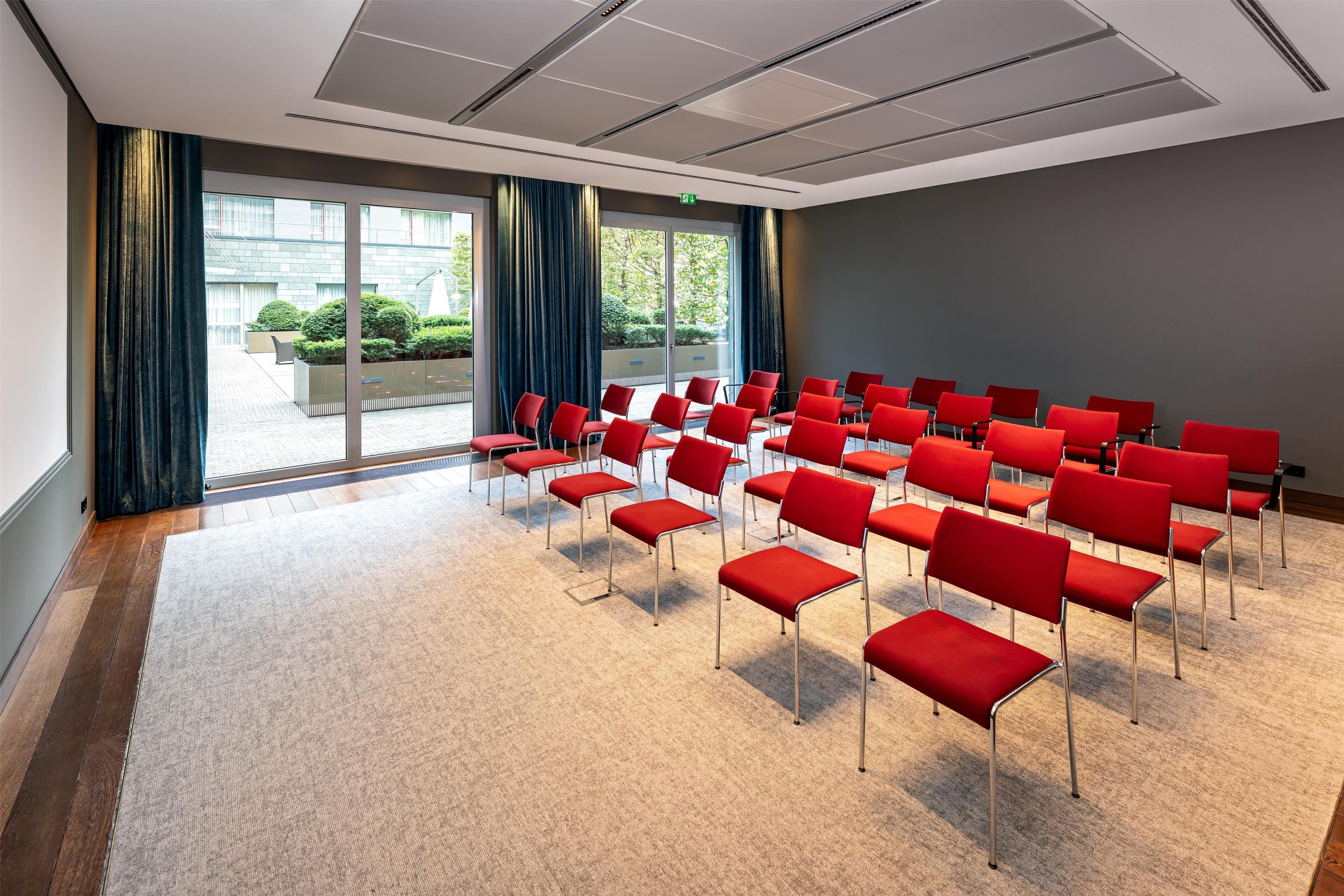A conference room with rows of red chairs, large windows, and a carpeted floor.