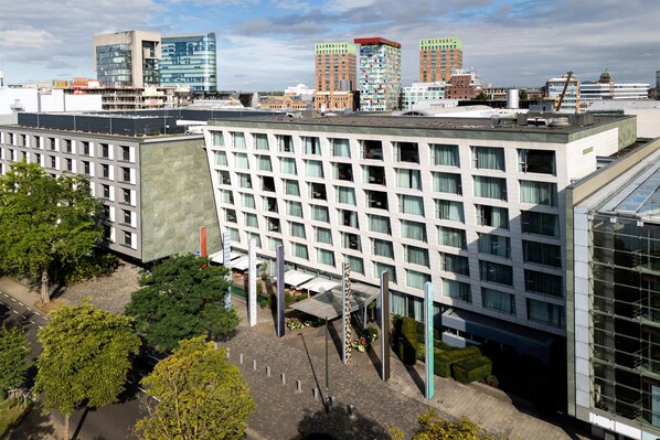 Un hotel moderno con una fachada de ventanas enrejada, un acceso cubierto y una terraza en la azotea.