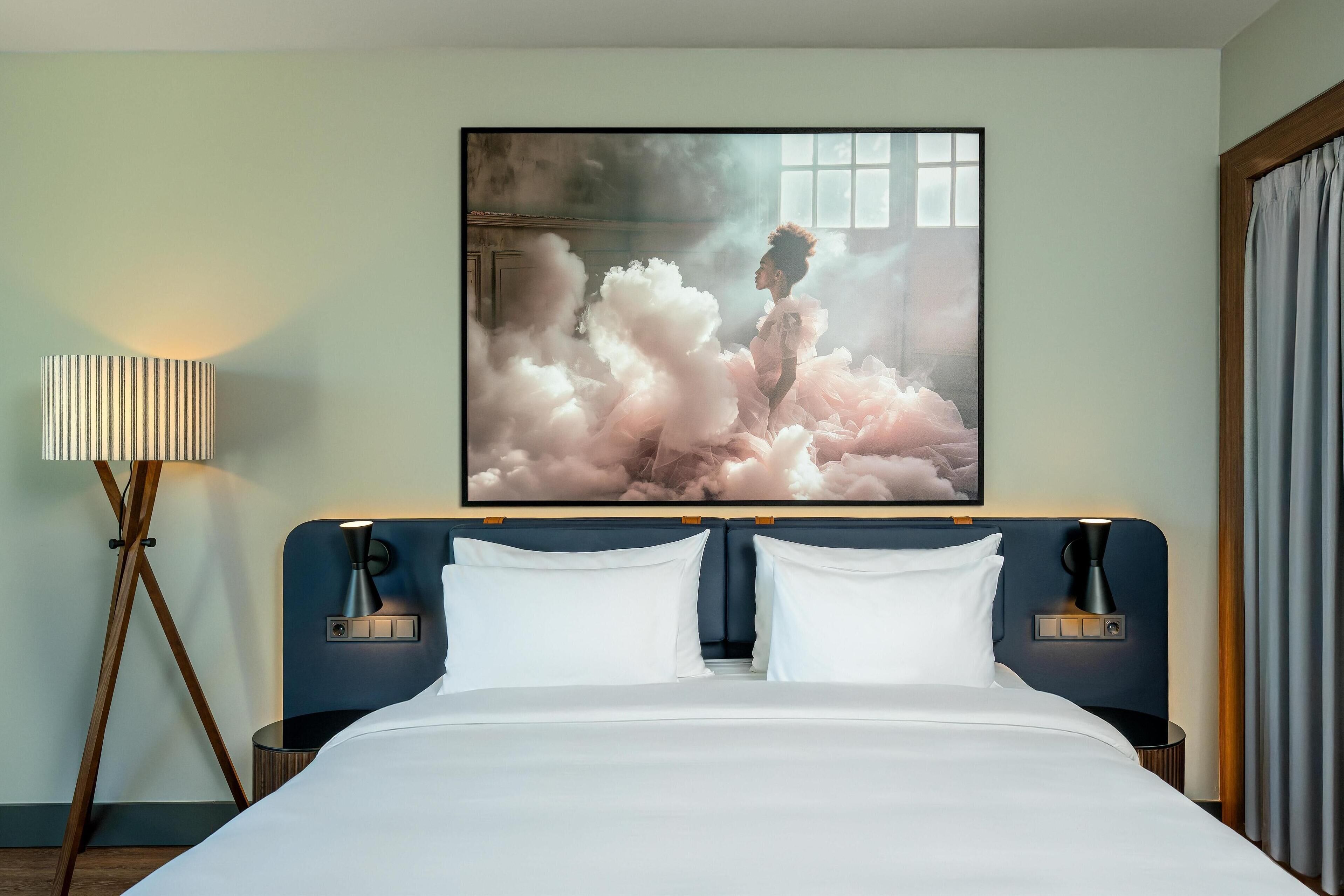Ein Hotelzimmer mit einem großen Bett, zwei Nachttischen, einer Stehlampe und einem großen Gemälde an der Wand.