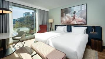 A hotel room with a large bed, a desk, a chair, a bench, a lamp, and a painting.