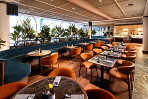 Un restaurante moderno con un sofá azul, sillas naranjas y mesas de madera.