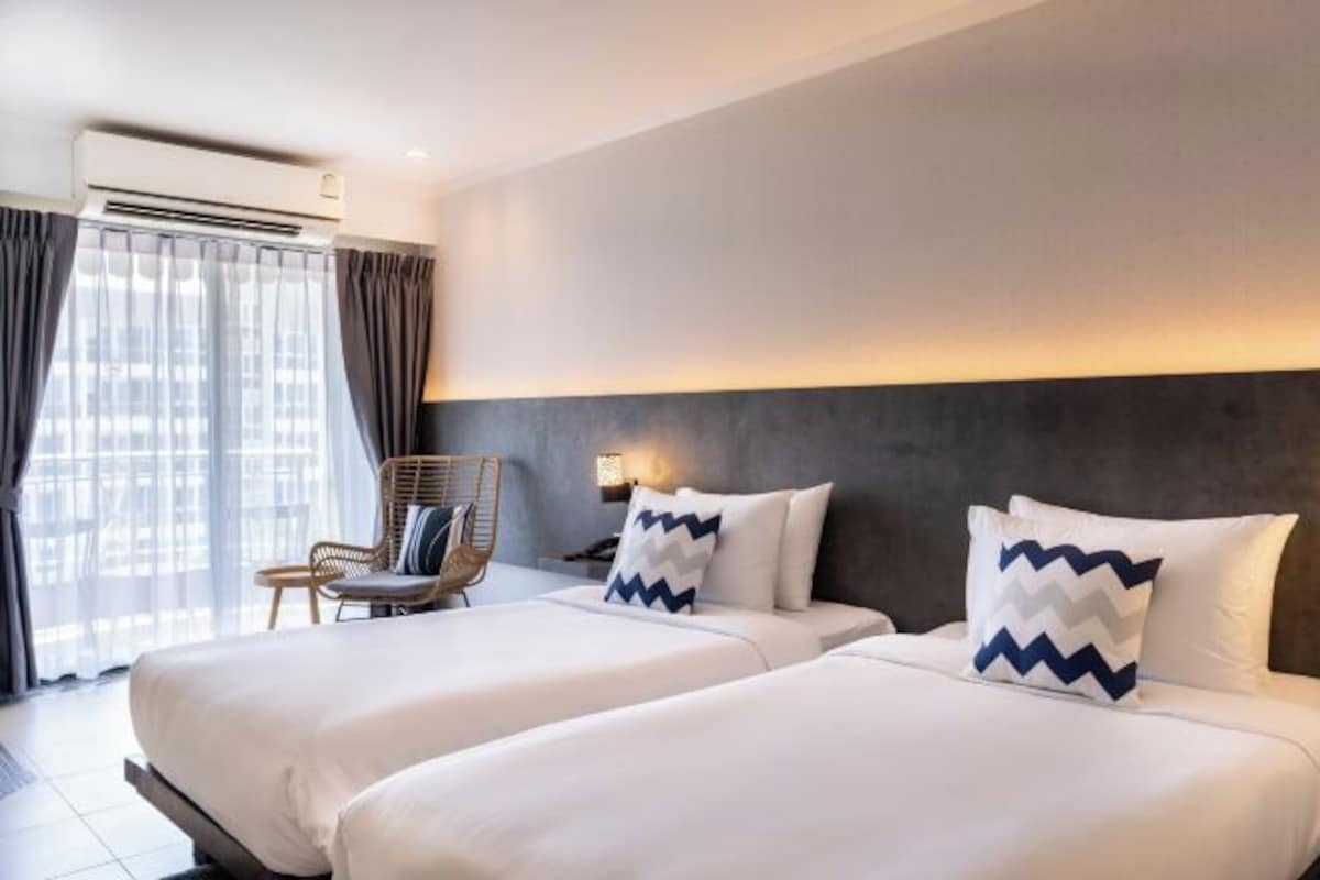Une chambre d’hôtel avec deux lits, une chaise et une grande fenêtre avec des rideaux.