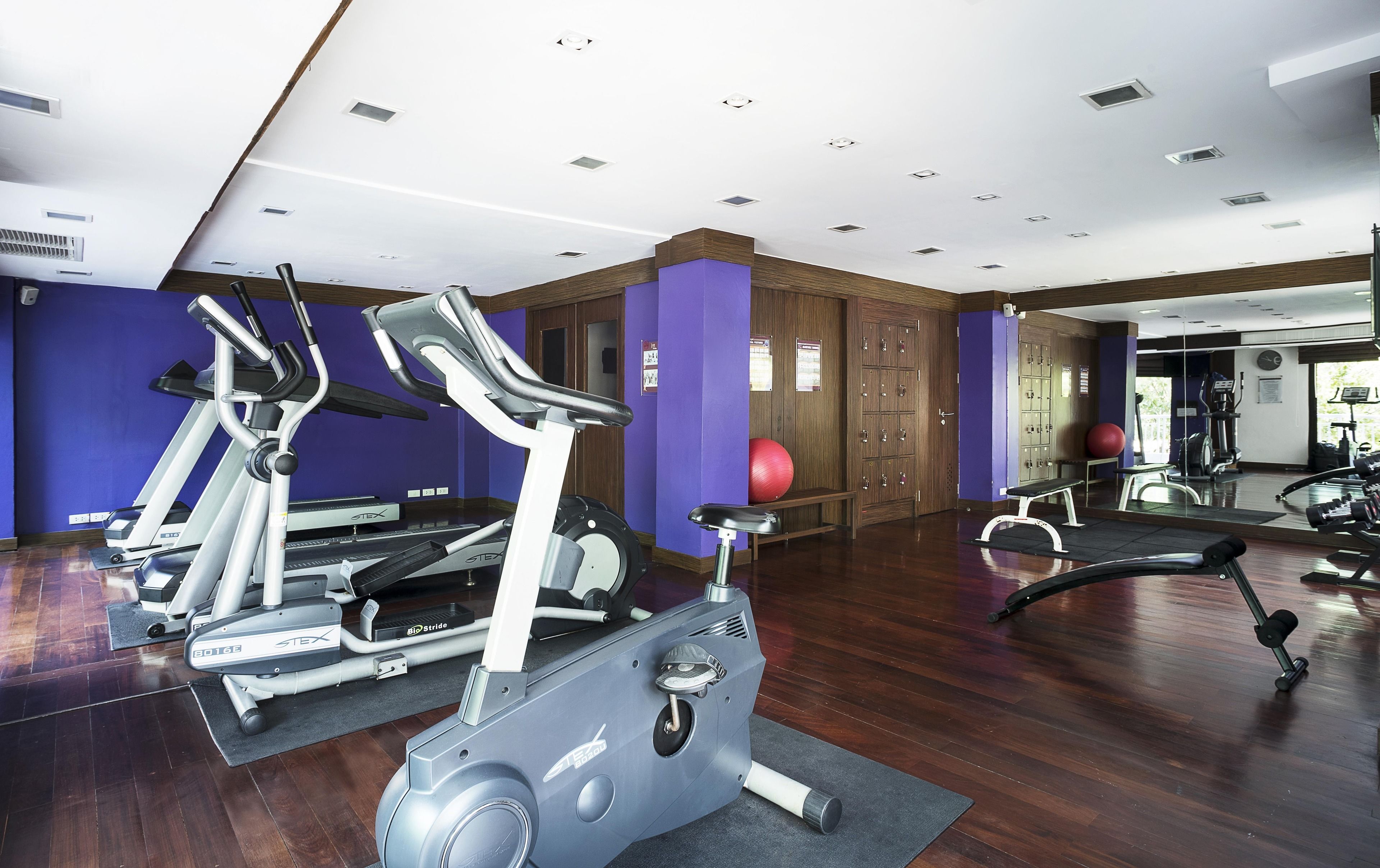Un gimnasio con cintas de correr, elípticas y una pelota de ejercicios roja.