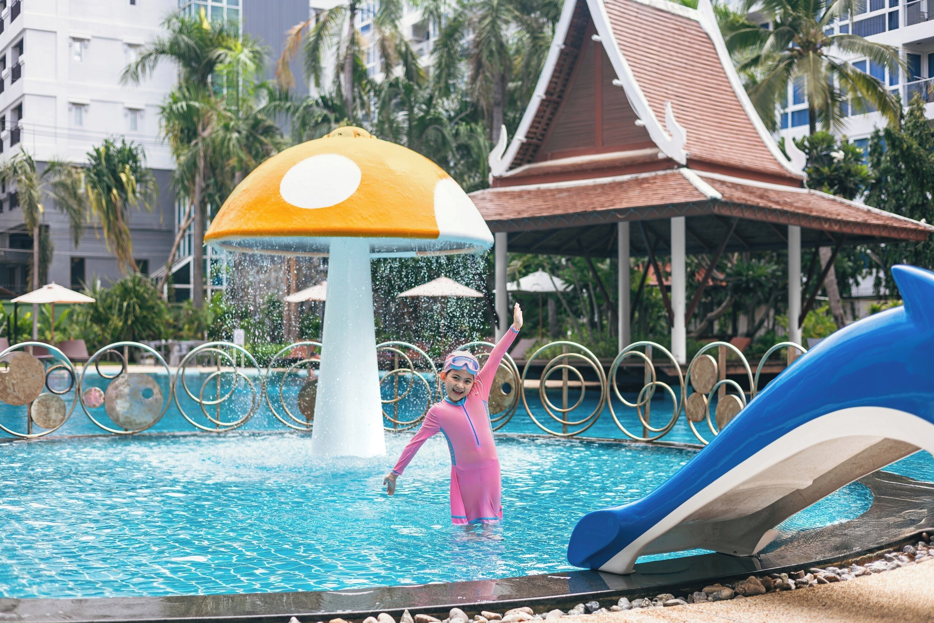 A pool area with a water feature, a slide, and a traditional building in the background.