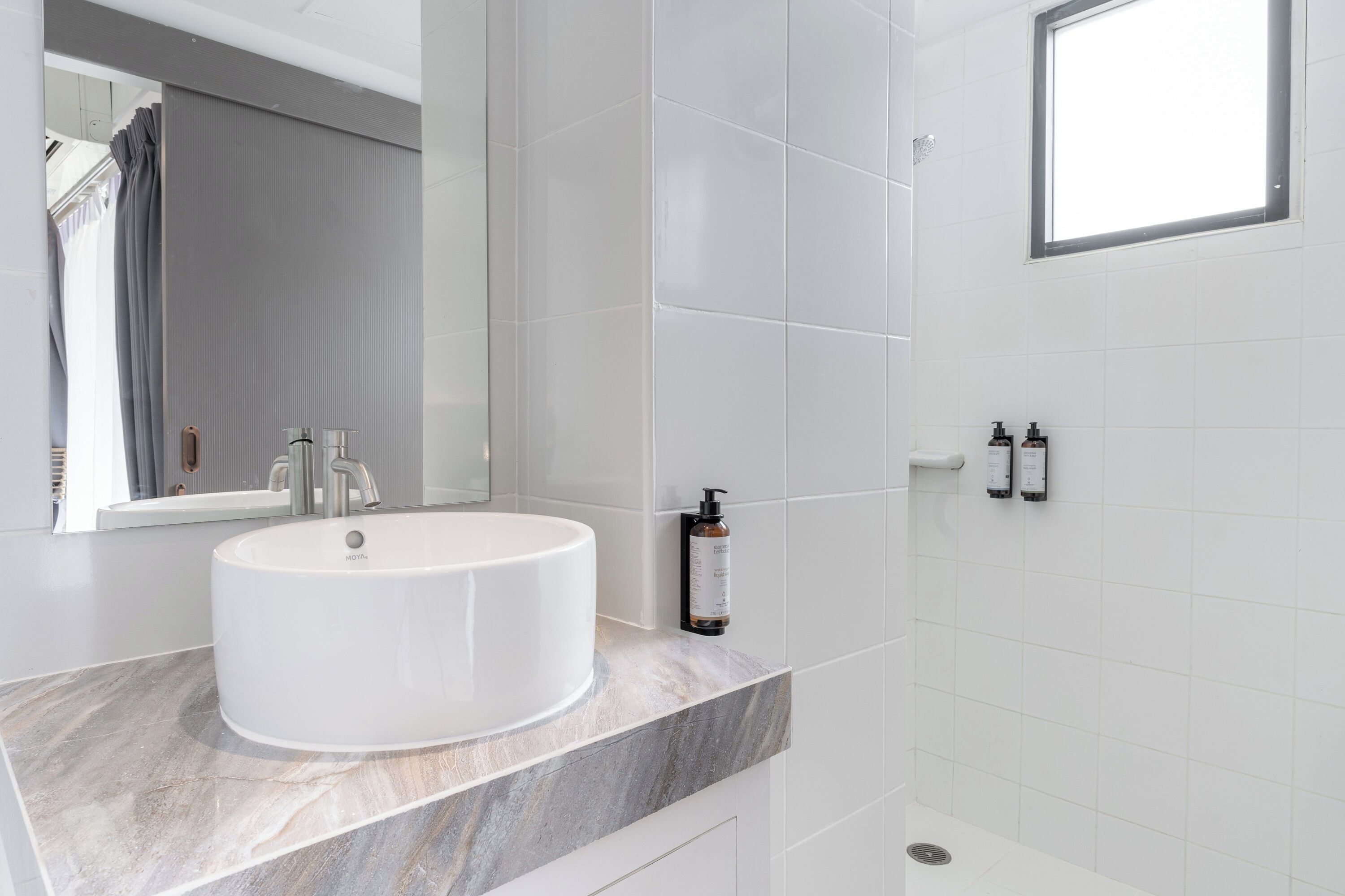 A modern bathroom with a white sink, marble countertop, and a large mirror.