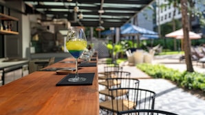 Un bancone in legno con un bicchiere di cocktail, posti a sedere all'aperto e una zona patio coperta.