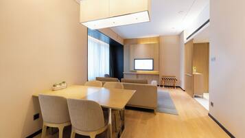 Una habitación de hotel moderna con comedor, sofá, televisor y una pequeña mesa con sillas.