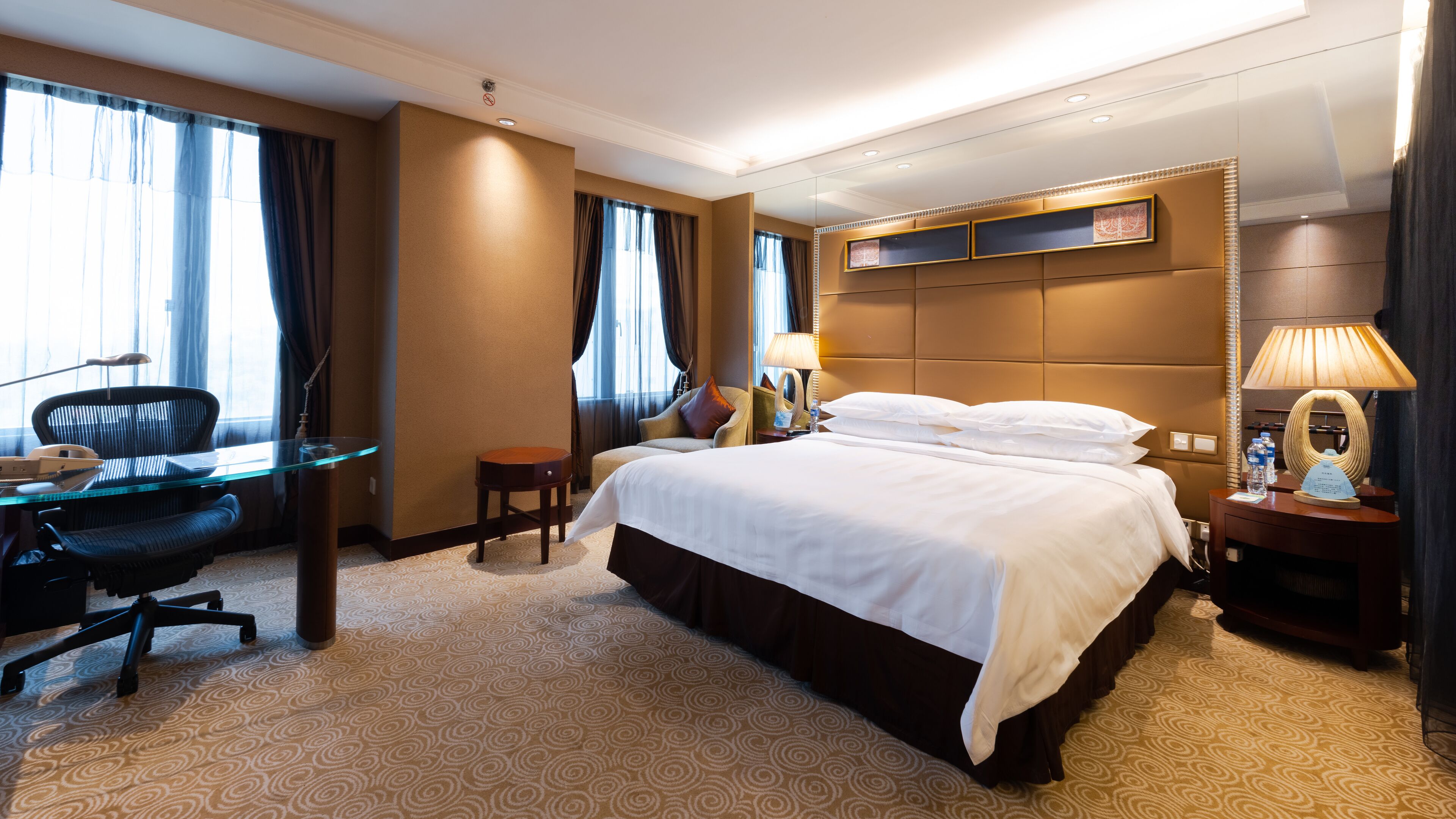Habitación de hotel con una cama grande, un escritorio con silla, una lámpara y un espejo.