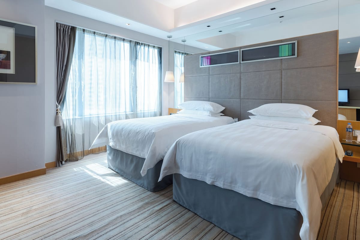 Ein Hotelzimmer mit zwei Betten, einem Schreibtisch, einem Stuhl, einem Fernseher und einem Fenster mit Vorhängen.