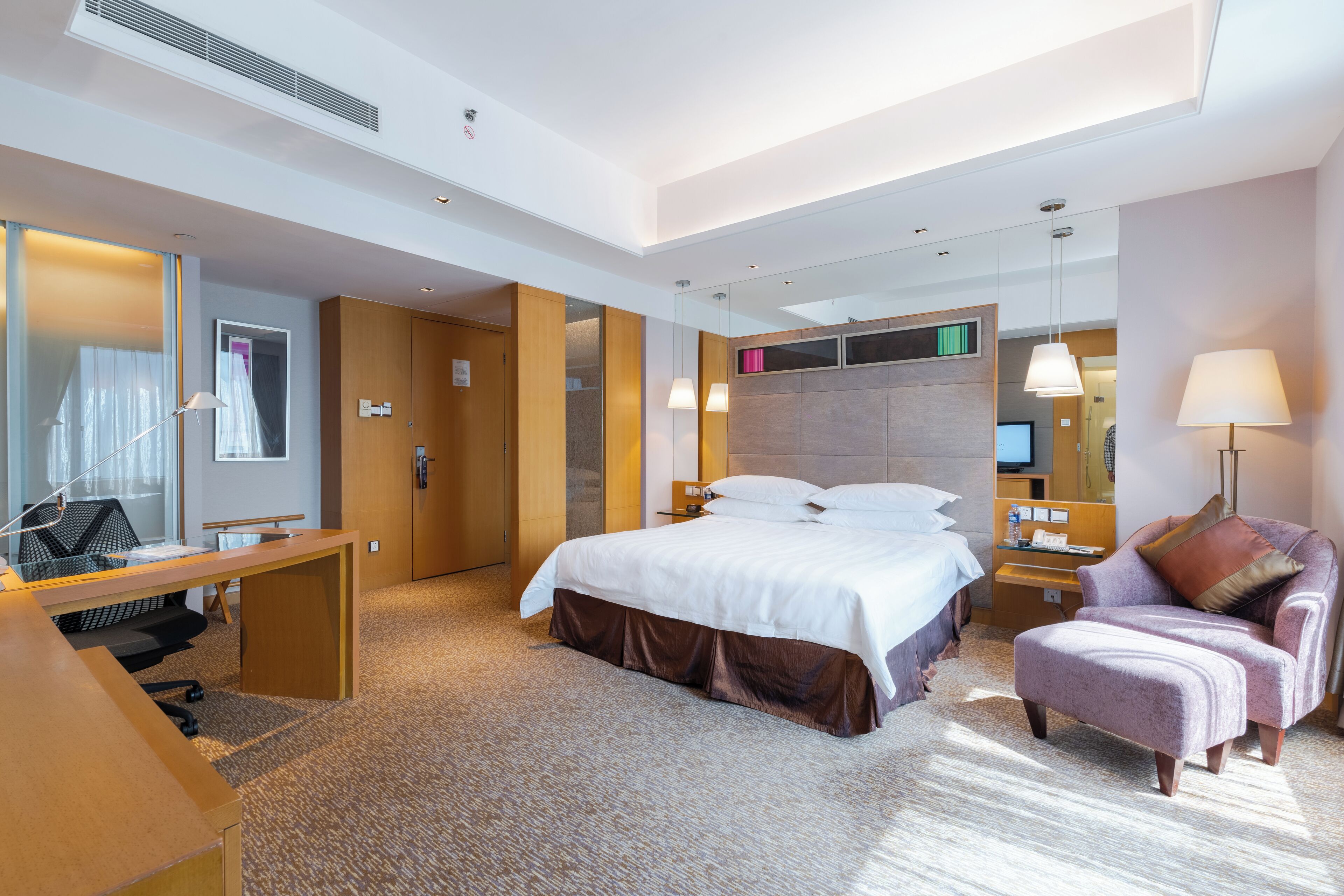 A hotel room with a bed, a desk, a chair, a TV, and a mirror.
