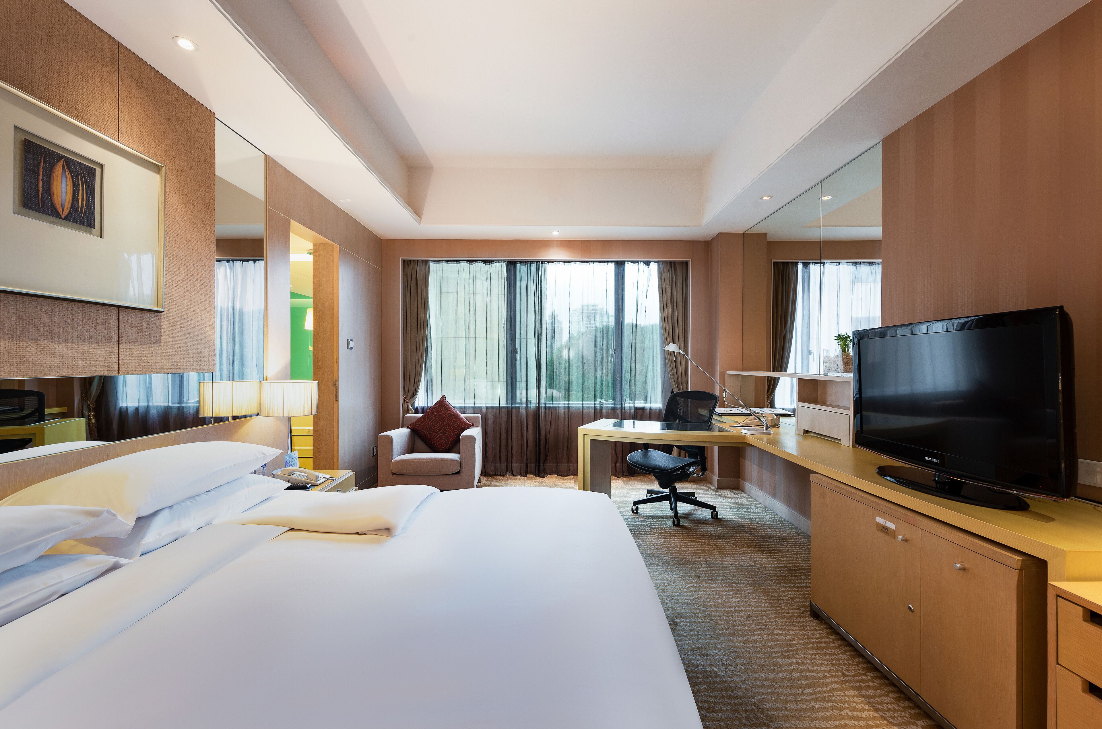 A hotel room with a large bed, a desk with a chair, a television, and a mirror.