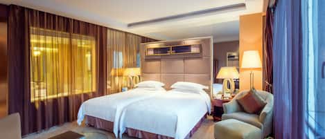 A hotel room with two beds, a sitting area with a chair, a small table, and a fruit plate.