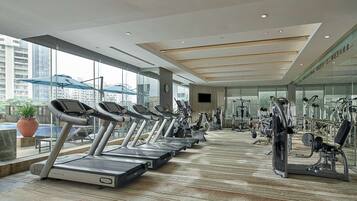Un gimnasio moderno con cintas de correr, elípticas y equipo de pesas. Amplias ventanas ofrecen vistas a la ciudad.