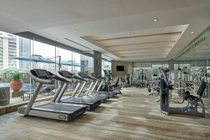 Un gimnasio moderno con cintas de correr, elípticas y equipo de pesas. Amplias ventanas ofrecen vistas a la ciudad.