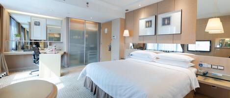 A modern hotel room with a large bed, a desk with a chair, a small table, a mirror, and a television.