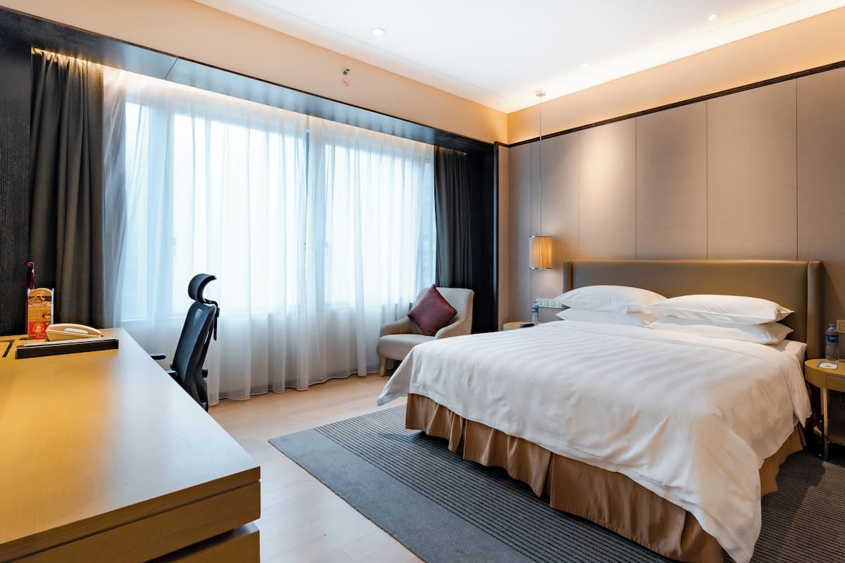 Ein modernes Hotelzimmer mit einem großen Bett, einem Schreibtisch, einem Stuhl und einem Nachttisch.
