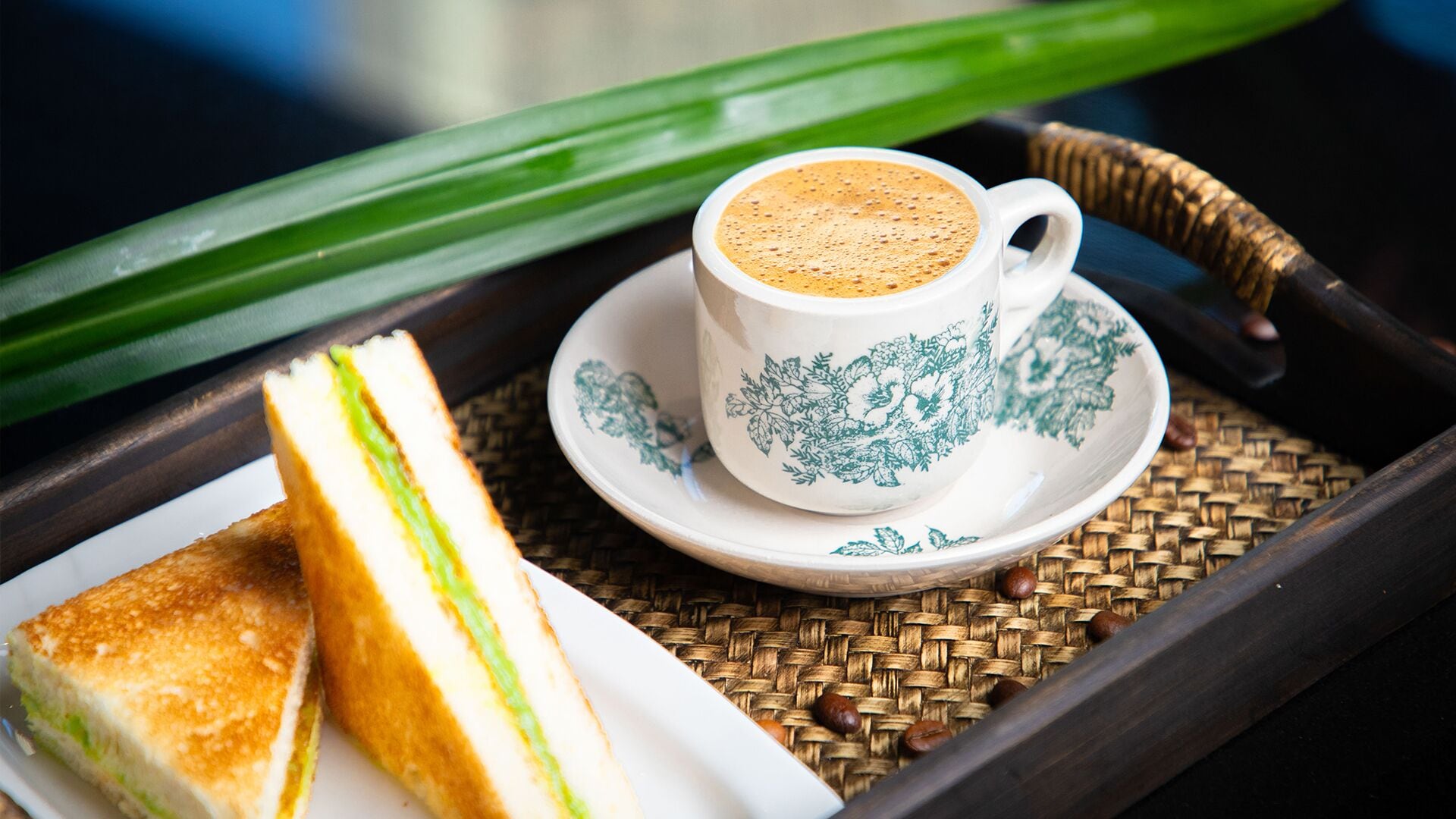 En bakke med en sandwich, en kop kaffe og et grønt blad.
