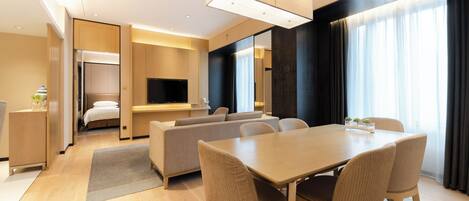 A modern hotel room with a dining area, a sofa, a TV, and a bed.