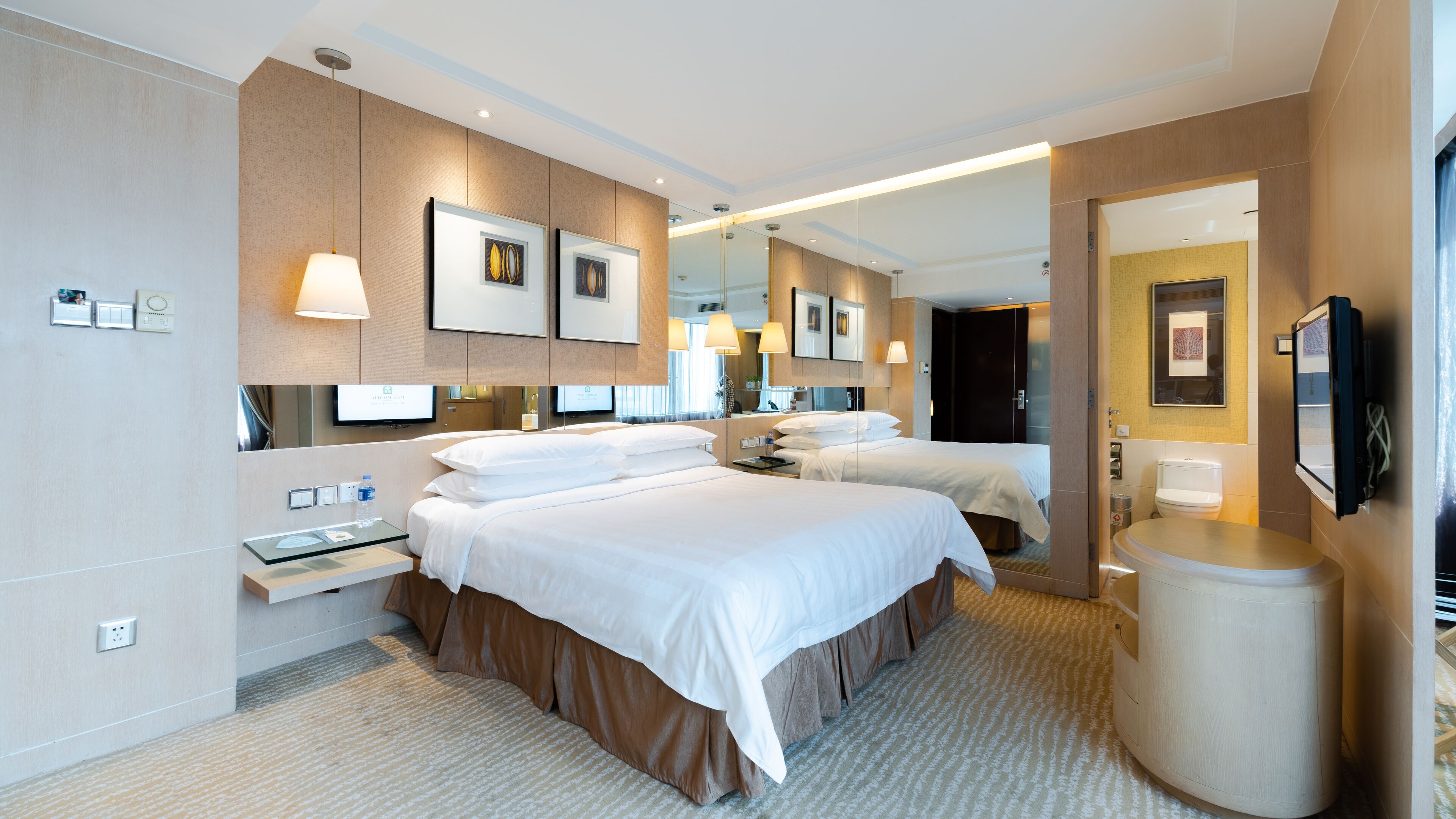 A hotel room with two beds, a desk, a mirror, and a TV.