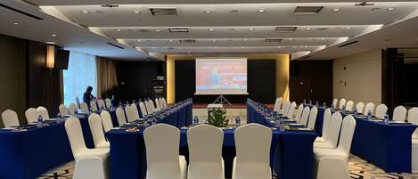 Una sala de conferencias con una larga mesa, sillas blancas y una pantalla mostrando una presentación.