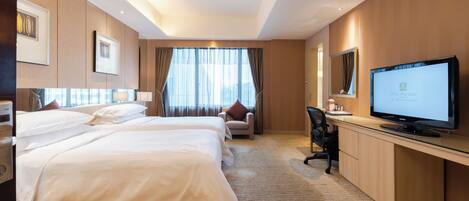 A hotel room with two beds, a desk with a computer, a television, and a large window with curtains.
