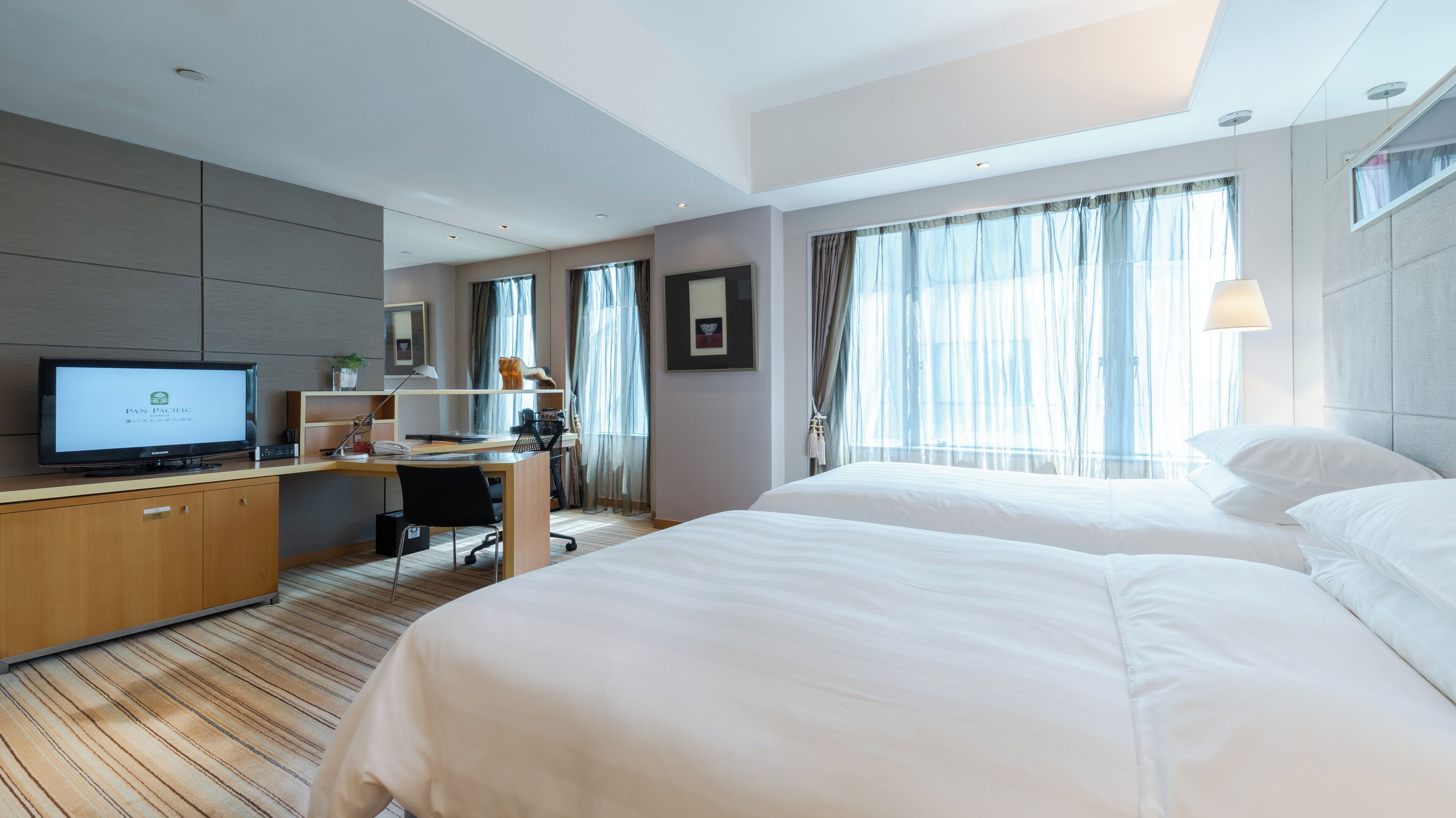 Habitación de hotel con cama, escritorio, computadora, televisor y ventana con cortinas.