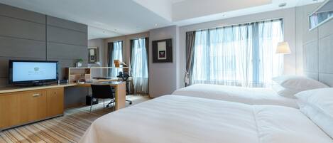 A hotel room with a bed, a desk with a computer, a television, and a window with curtains.