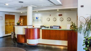 A hotel reception area with a reception desk, clocks displaying different time zones, and a sign for the Galleria Hotel. - Hotel Gallia (Pianezza)