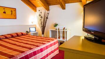 Habitación de hotel con cama, escritorio con computadora, televisión y un florero con ramas.