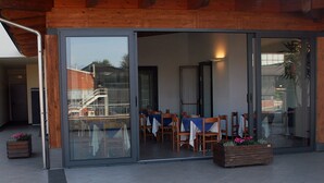 A modern building with a glass entrance, wooden exterior, and outdoor seating area with tables and chairs. - Hotel Gallia (Pianezza)