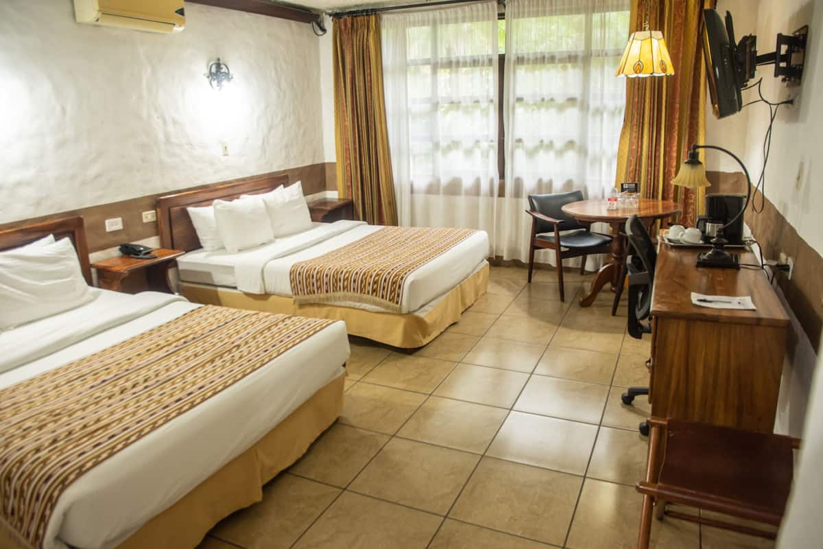 A hotel room with two beds, a desk, a chair, a lamp, and a TV.